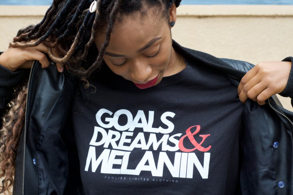 Image of a woman wearing a shirt saying "goals dreams & melanin" which is similar to the empowerment that is given in black female therapy. Women of color therapy in Atlanta with black female therapists can help you embrace your identity, voice, & culture.