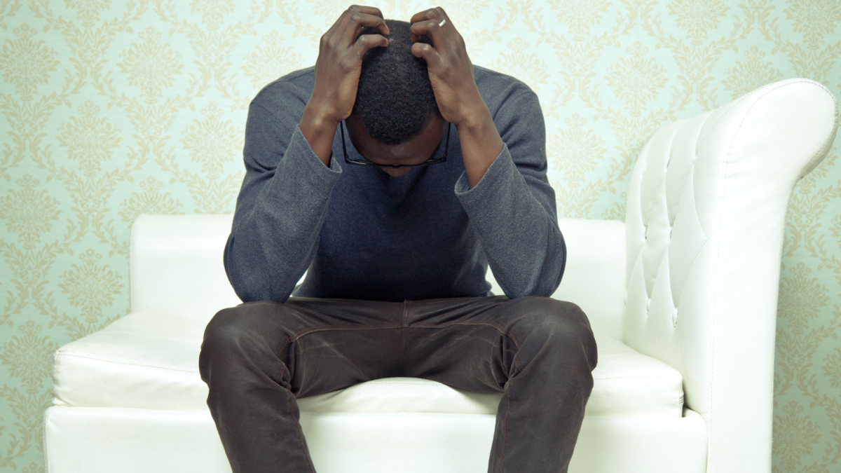 Image of a Black man with his head hanging down. Representing someone who is in need of grief and loss counseling with a grief counselor in Atlanta, GA.