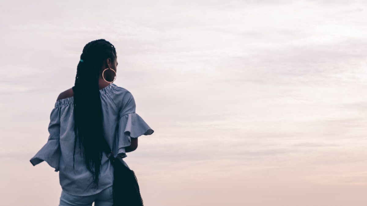 Image of a Back woman staring out at the pink sky. Representing someone who could benefit from ACT therapy in Atlanta, Georgia. With support of a therapist ACT for anxiety can give you freedom.