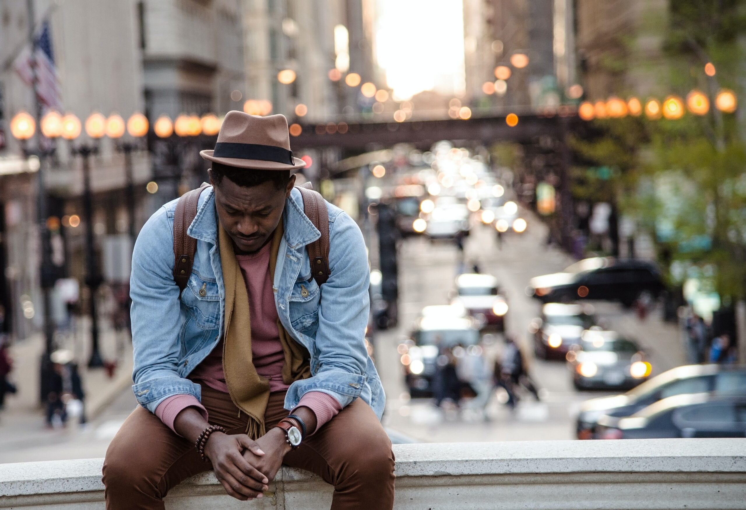 Image of a Black man sitting outside on a raised ledge. Representing someone who is showing signs of grief and could benefit of support of an Atlanta grief counselor. Where with grief counseling he can feel better.