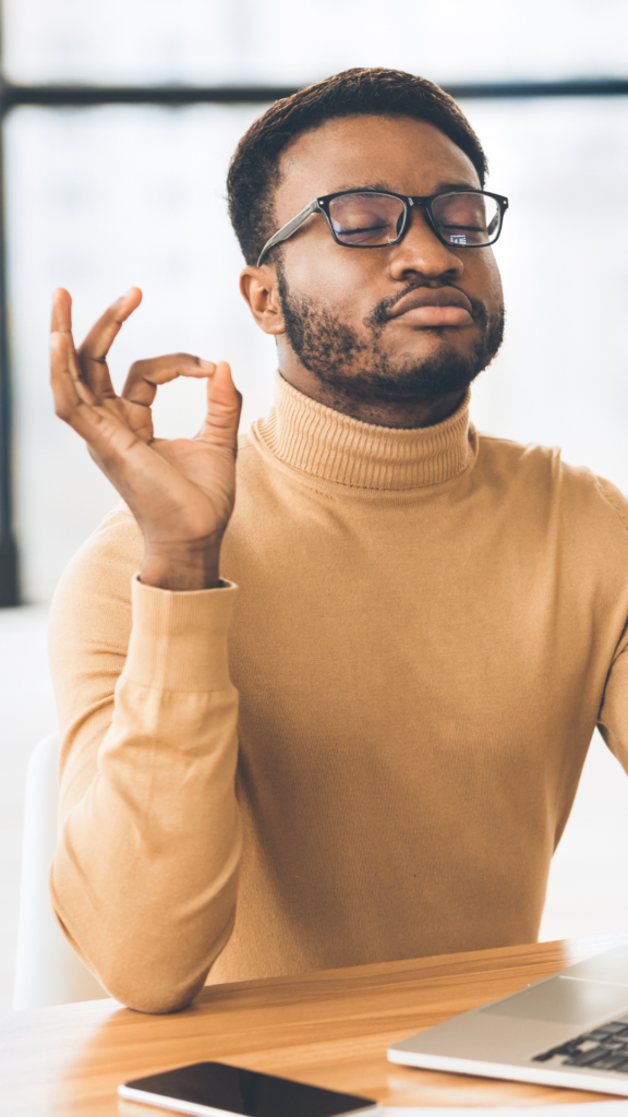 Image of a Black man in a yellow shirt taking deep breaths while working. Representing someone who could benefit from seeing an Atlanta therapist for their anxiety symptoms. Anxiety therapy can provide you with the help you need.