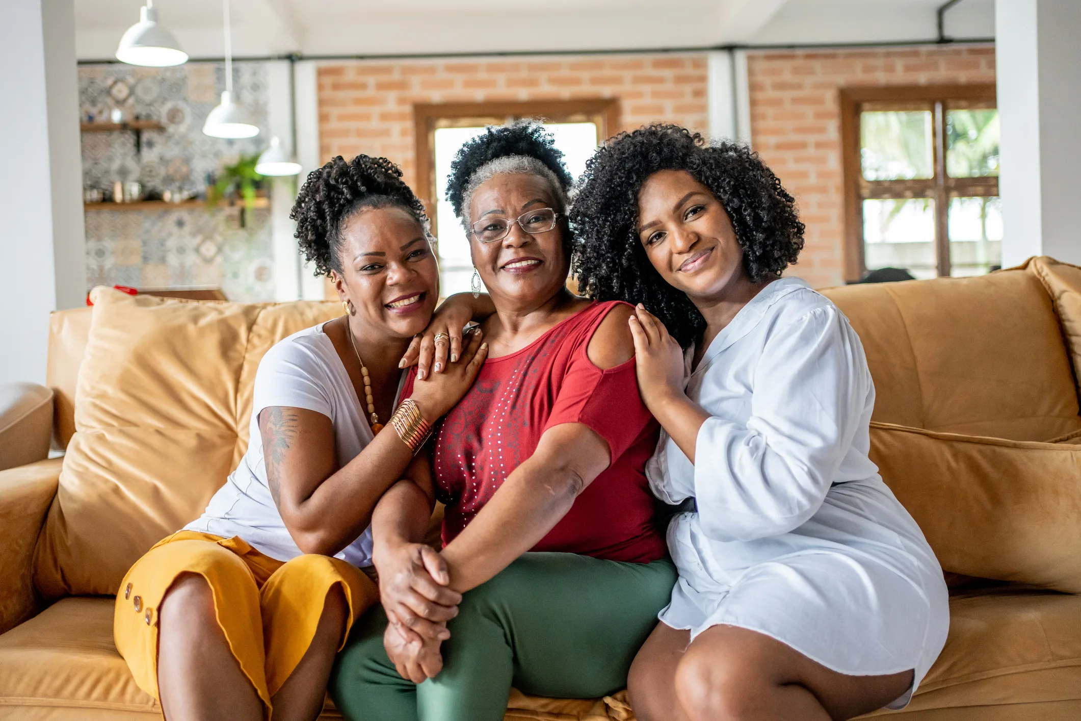 Portrait of mother with her daughters sitting close and hugging on yellow couch