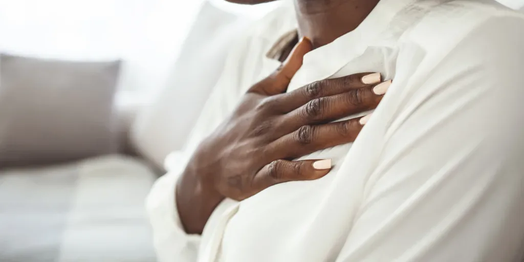 Image of Black woman practicing deep breathing touching chest sitting on a couch in the living room at home. Representing therapy technique to manage anxiety with an Atlanta therapist.